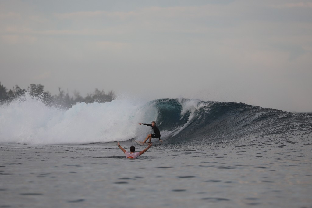 Surfer riding inside a breaking wave while a coach celebrates from the water